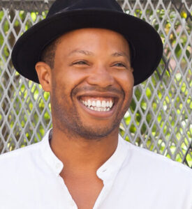 Marcel wearing a black hat and white shirt, smiling broadly