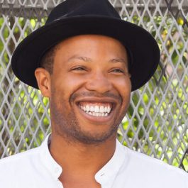 Marcel wearing a black hat and white shirt, smiling broadly