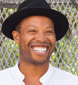 Marcel wearing a black hat and white shirt, smiling broadly
