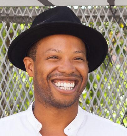 Marcel wearing a black hat and white shirt, smiling broadly